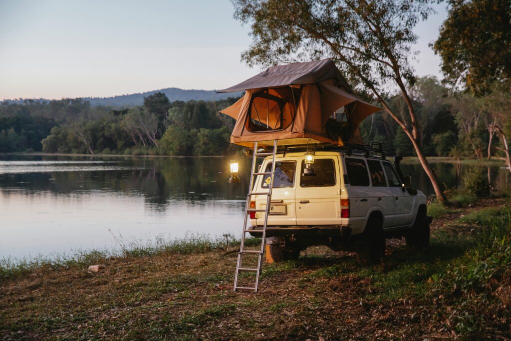 Camping tent with glowing retro lamps placed on top of white off road vehicle